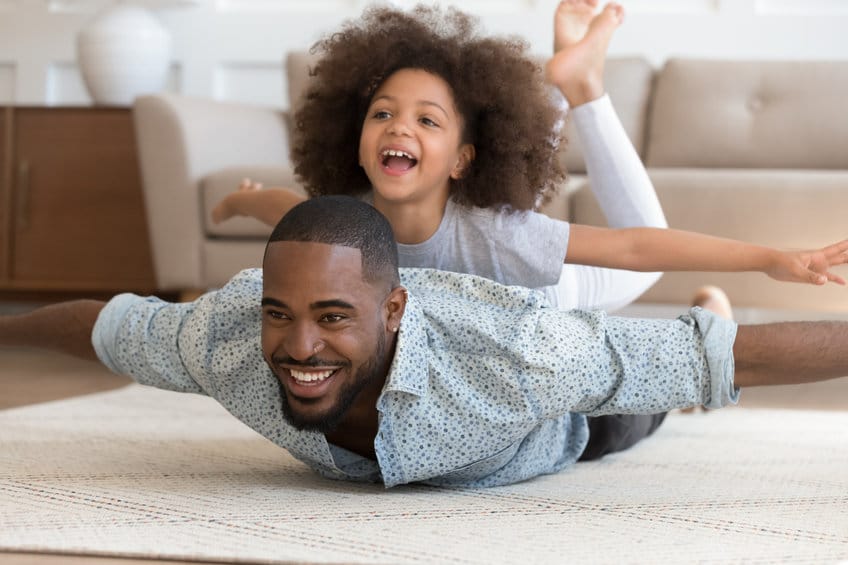 Happy black dad lying on floor with daughter on back.